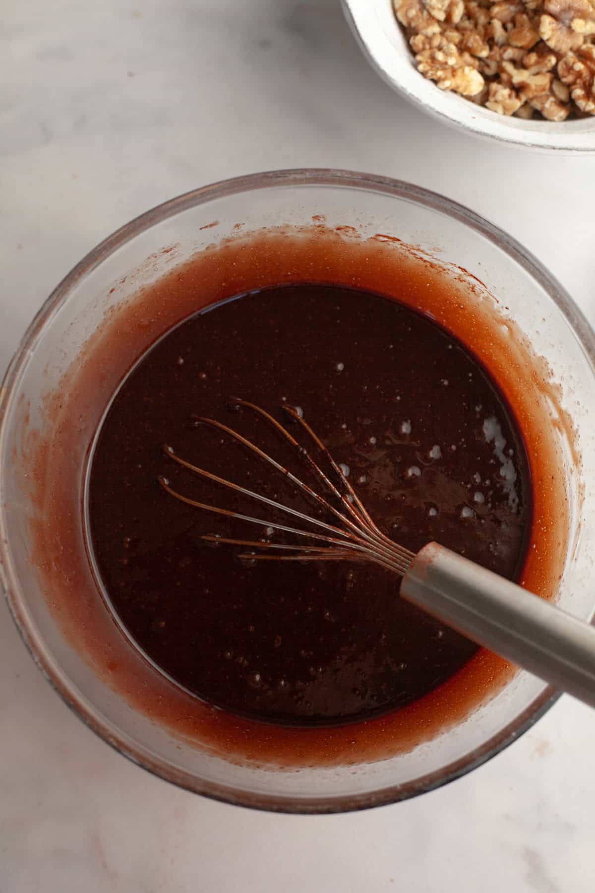 Brownie batter in a glass bowl with a whisk.