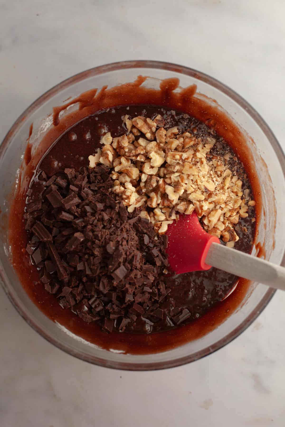 Brownie batter in a glass bowl with chopped chocolate and toasted walnuts.