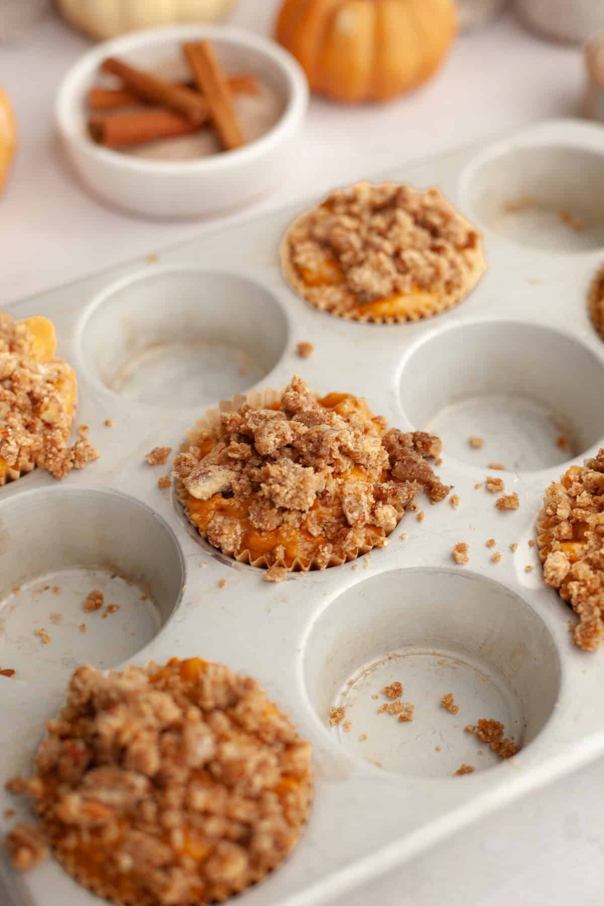 Unbaked pumpkin muffins with streusel in a muffin pan.