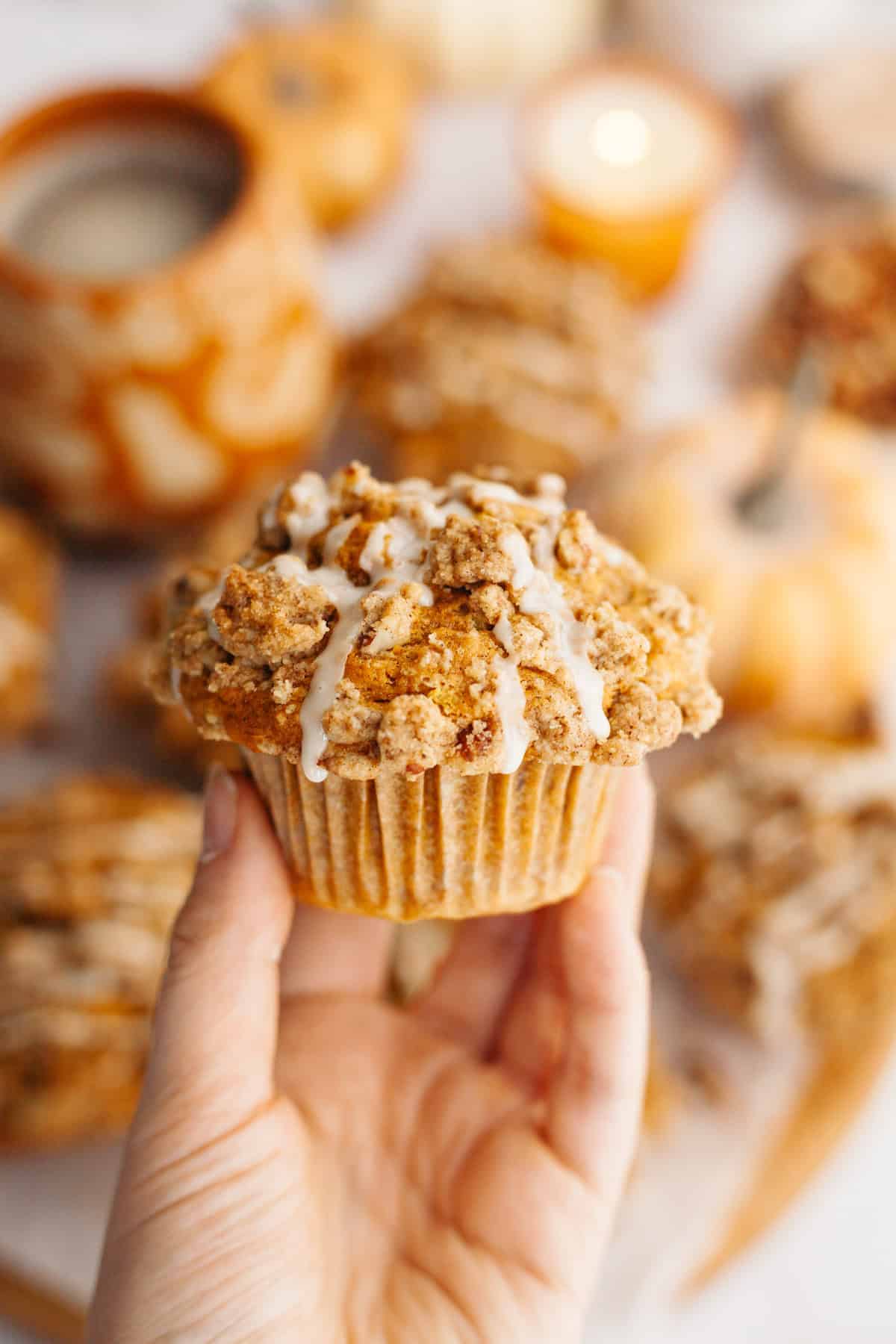 A hand holding a pecan pumpkin muffin with a white glaze.