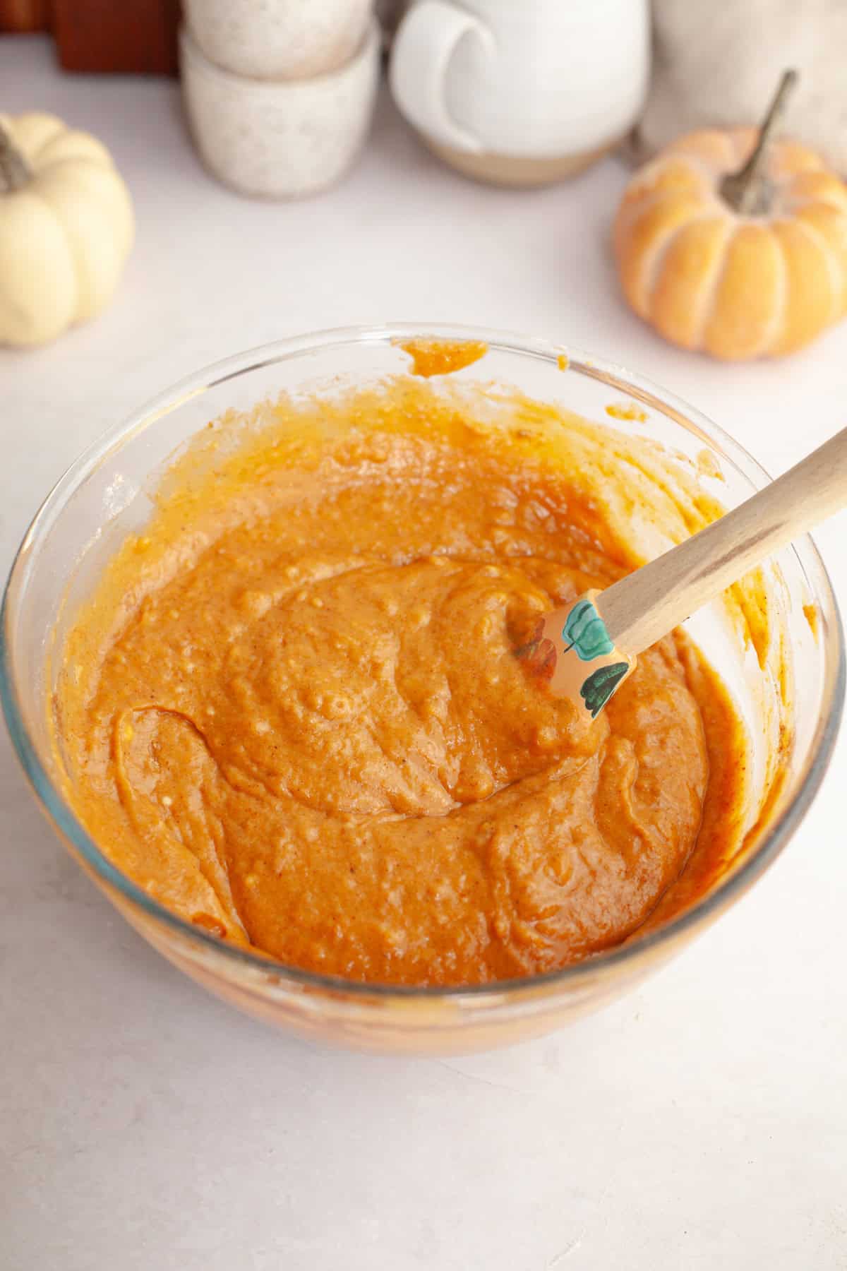 Pumpkin muffin batter in a glass bowl with a rubber spatula.