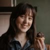 A woman with brown hair holding a cupcake. 