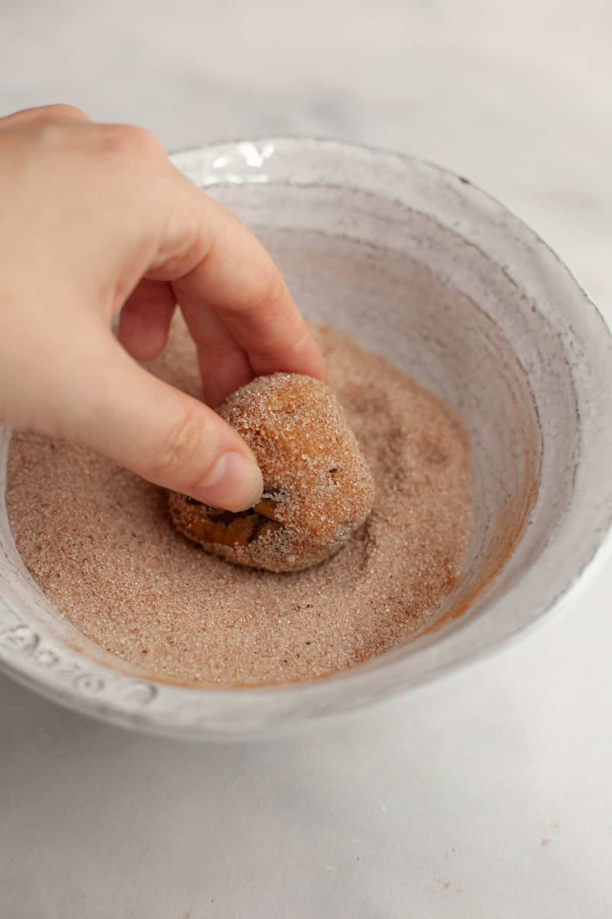 A hand rolling a cookie dough ball in pumpkin spice sugar.