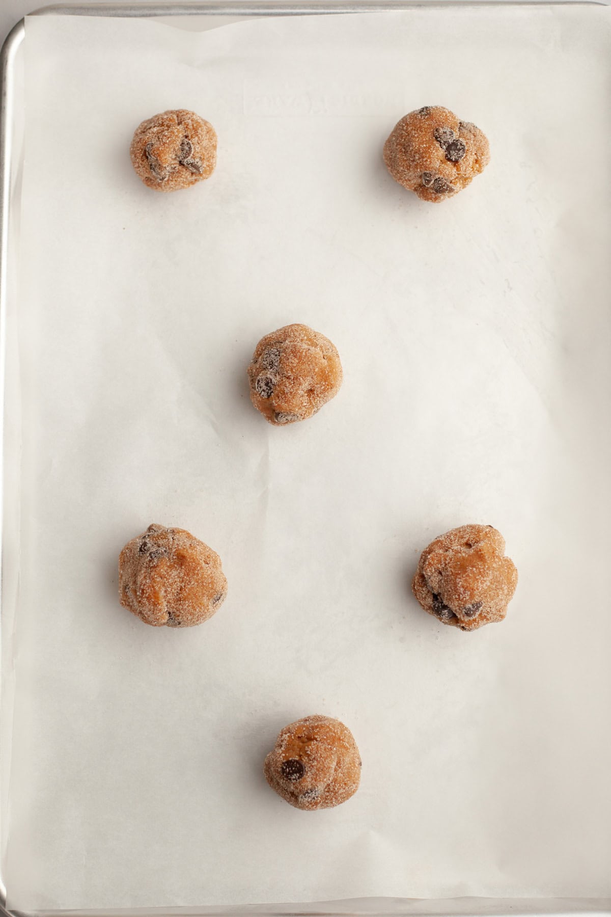 Cookie dough balls rolled in sugar on parchment paper on a baking sheet.