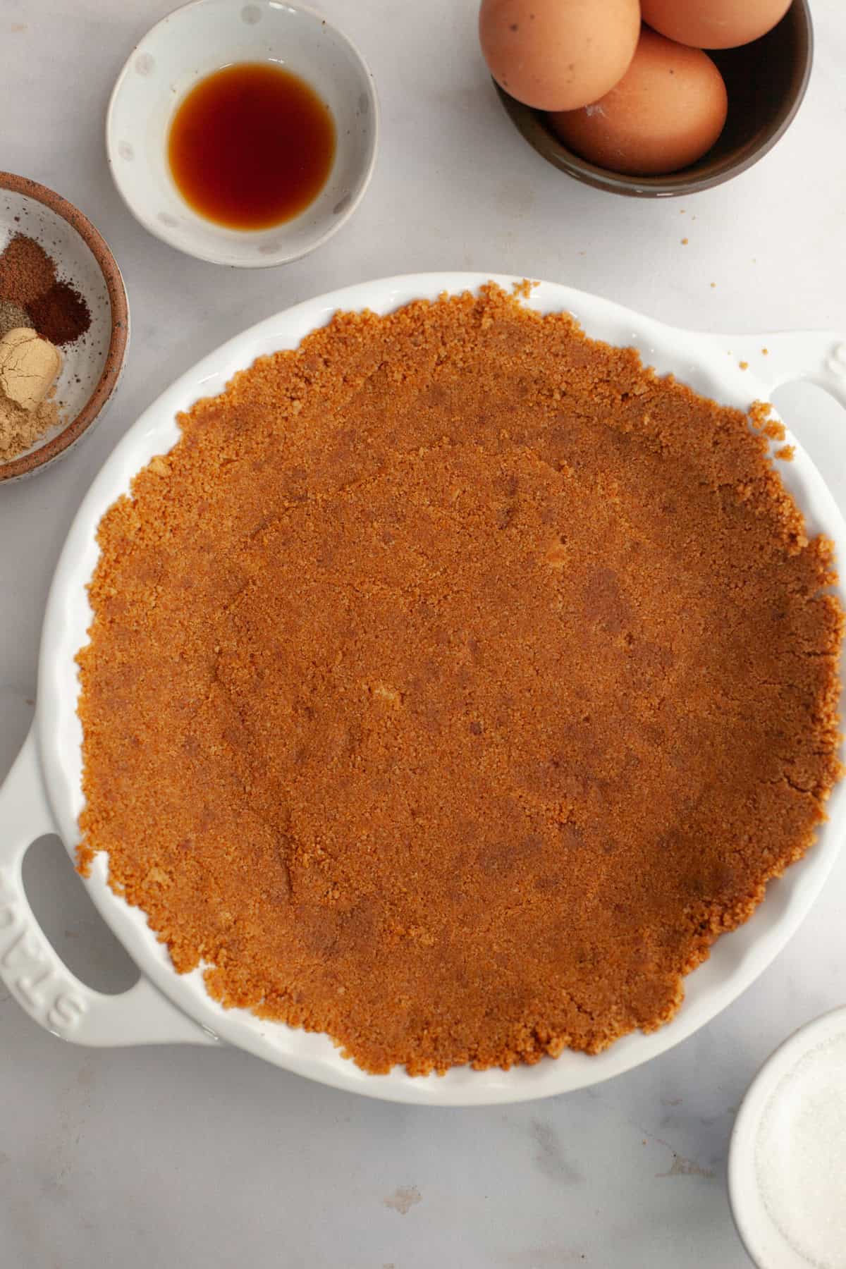 A white ceramic pie dish with a gingersnap crust in it.