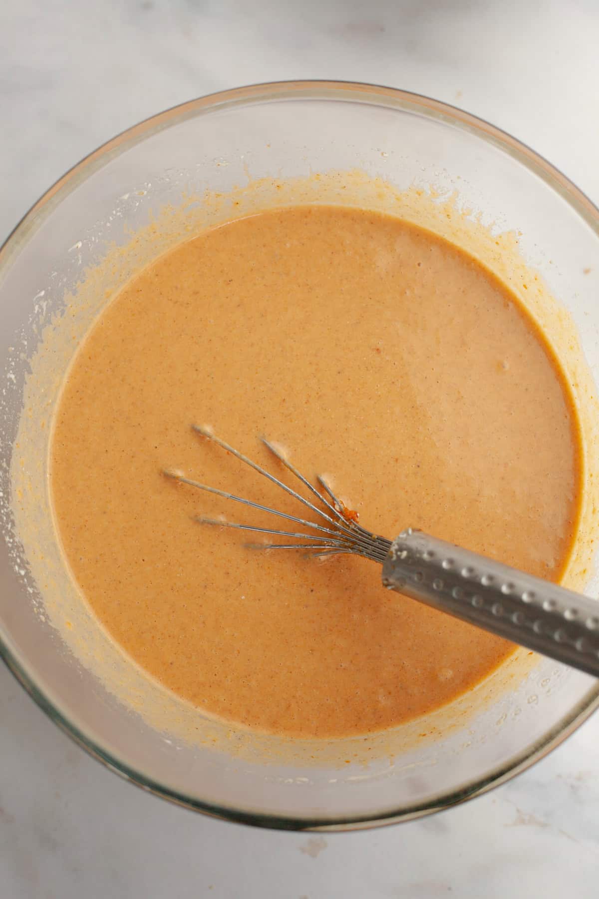 Pumpkin pie filling in a glass bowl with a whisk.