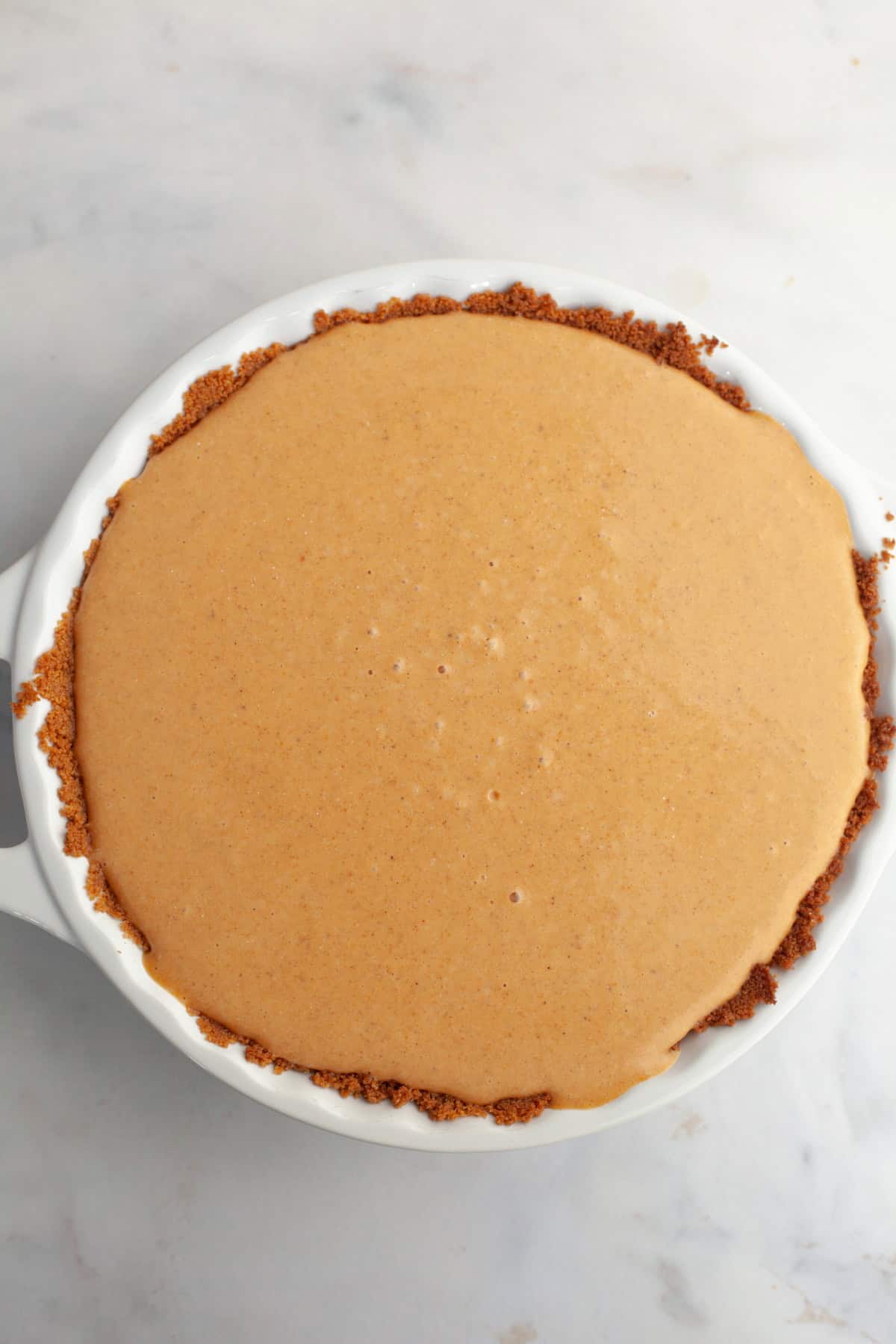 An unbaked pumpkin pie in a white ceramic baking dish.