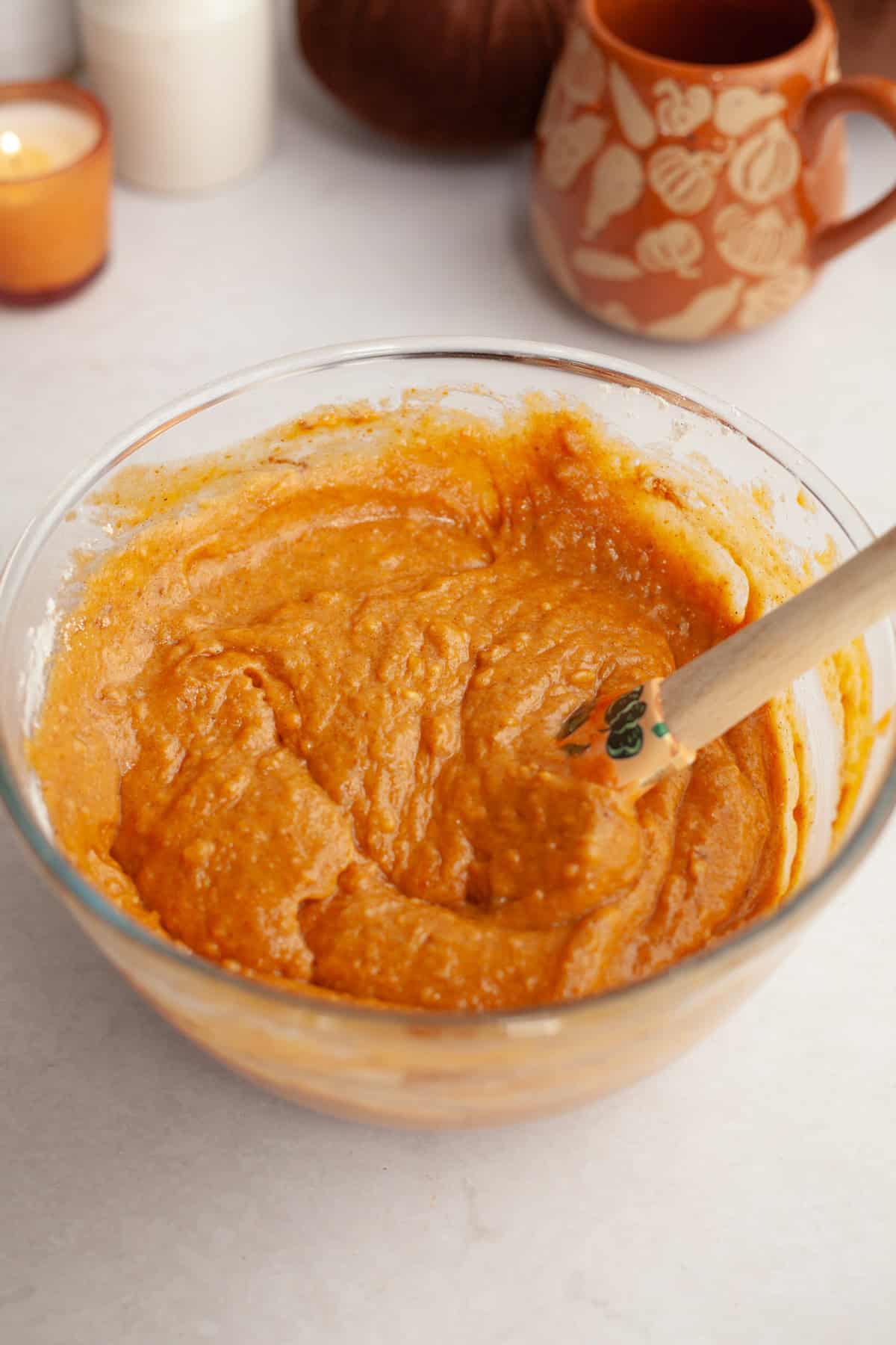 Pumpkin cake batter in a glass bowl with a rubber spatula.