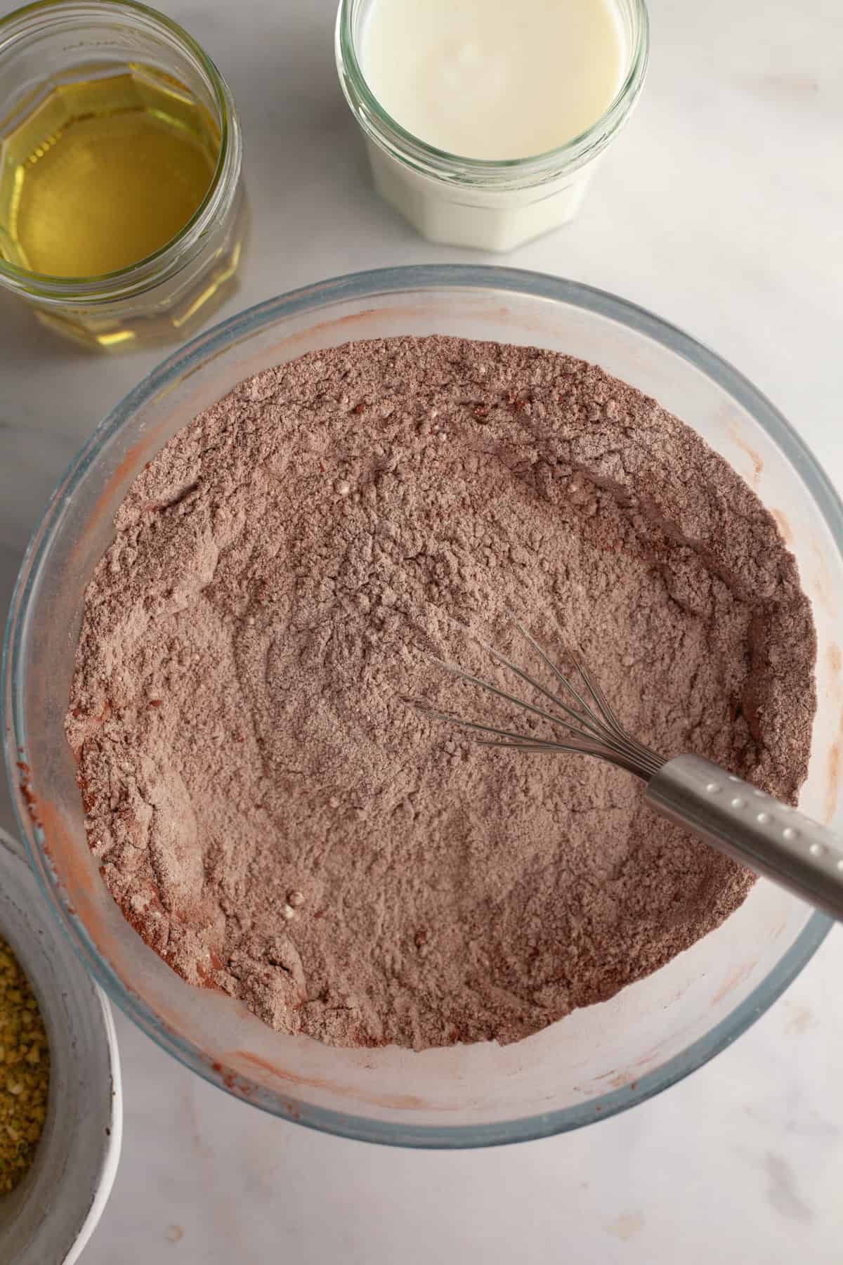 A bowl with a whisk and flour and cocoa powder.