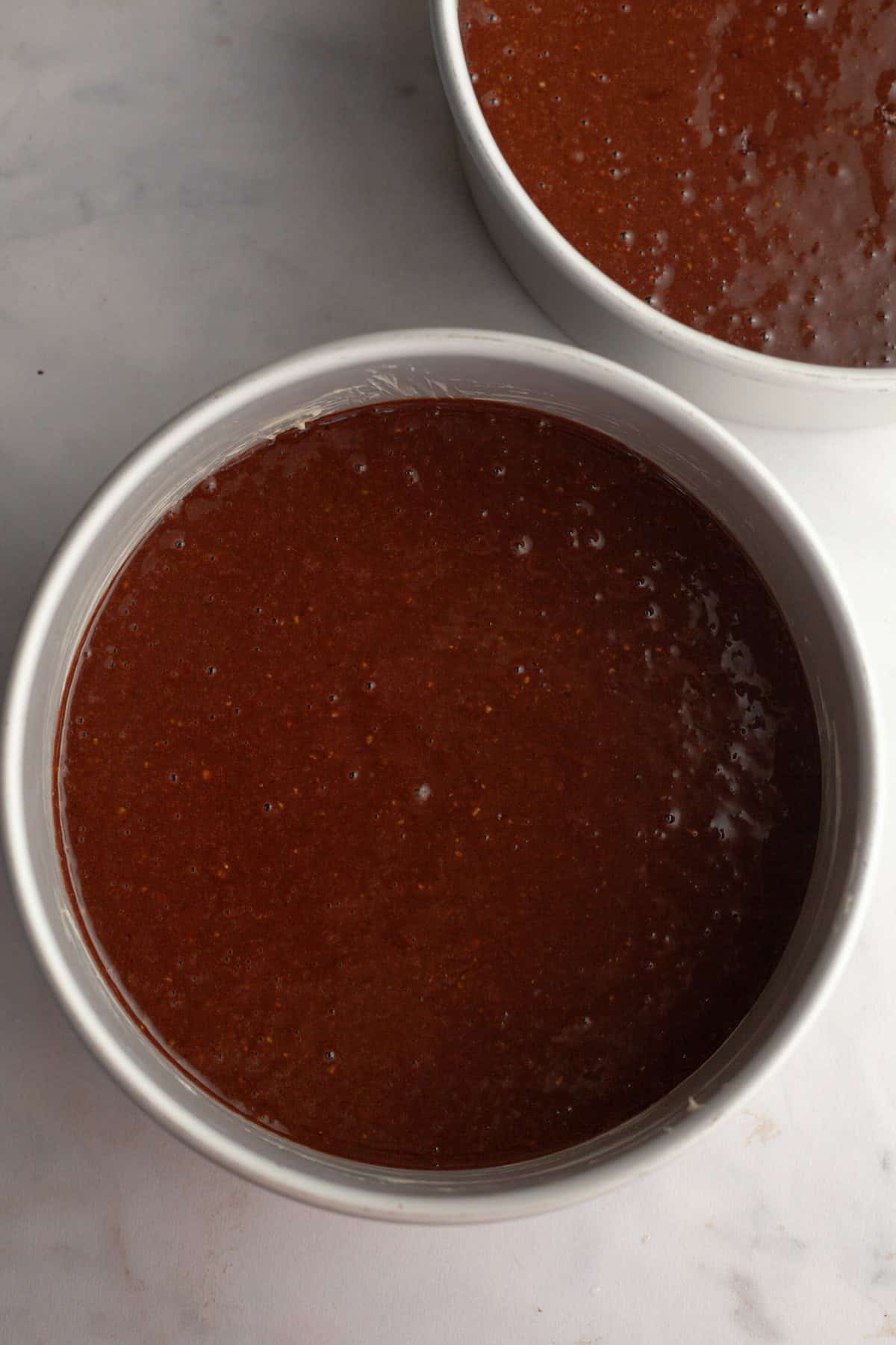 Two round cake pans with unbaked chocolate cake batter.