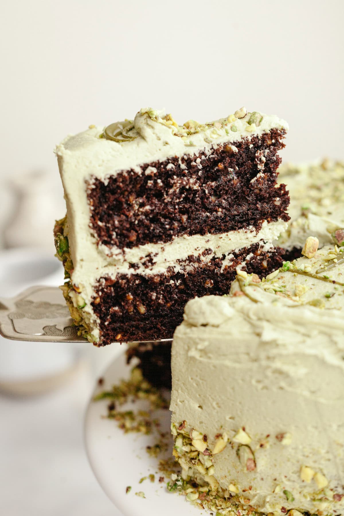 A slice of chocolate pistachio cake being lifted out with a silver cake server.