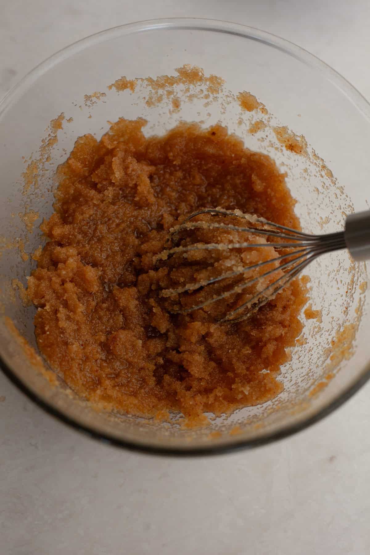 A glass bowl with a whisk and sugar and butter mixed together.