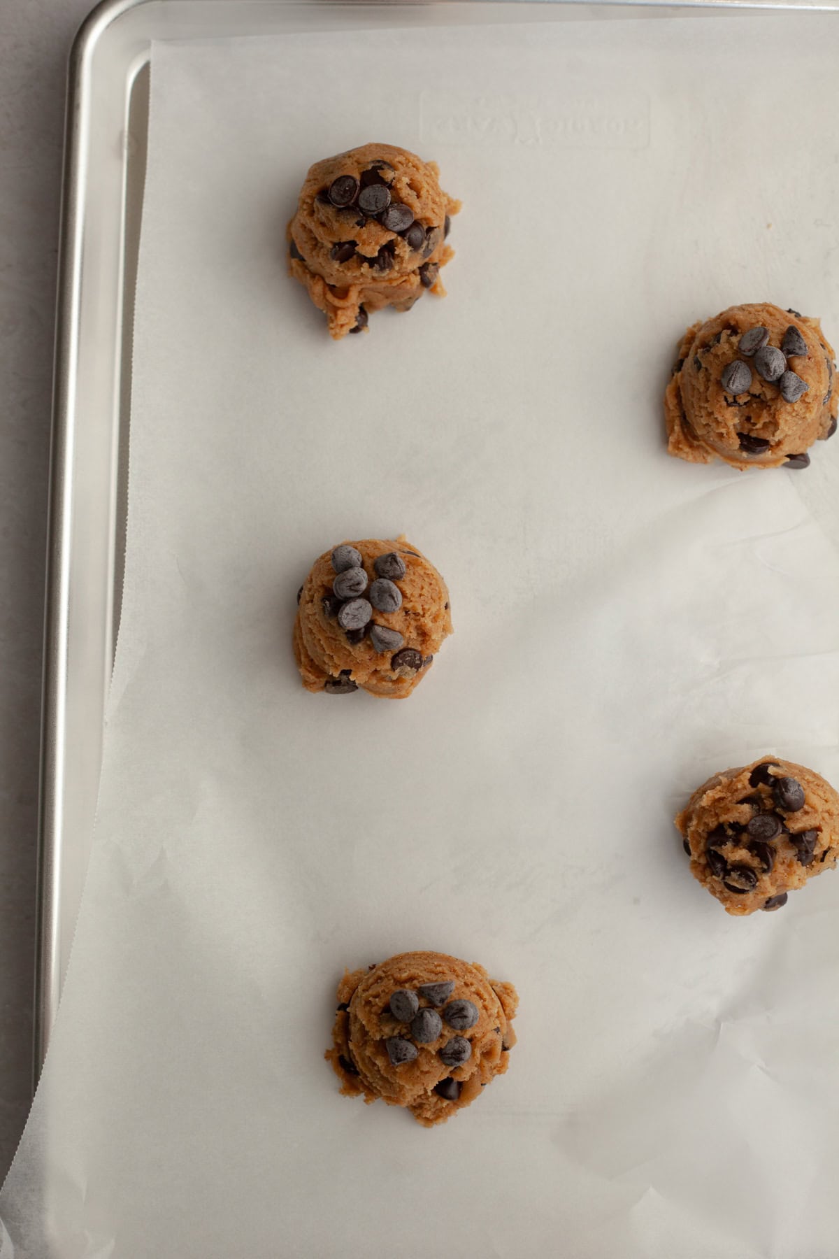 Chocolate chip cookie dough balls on a parchment lined baking sheet.