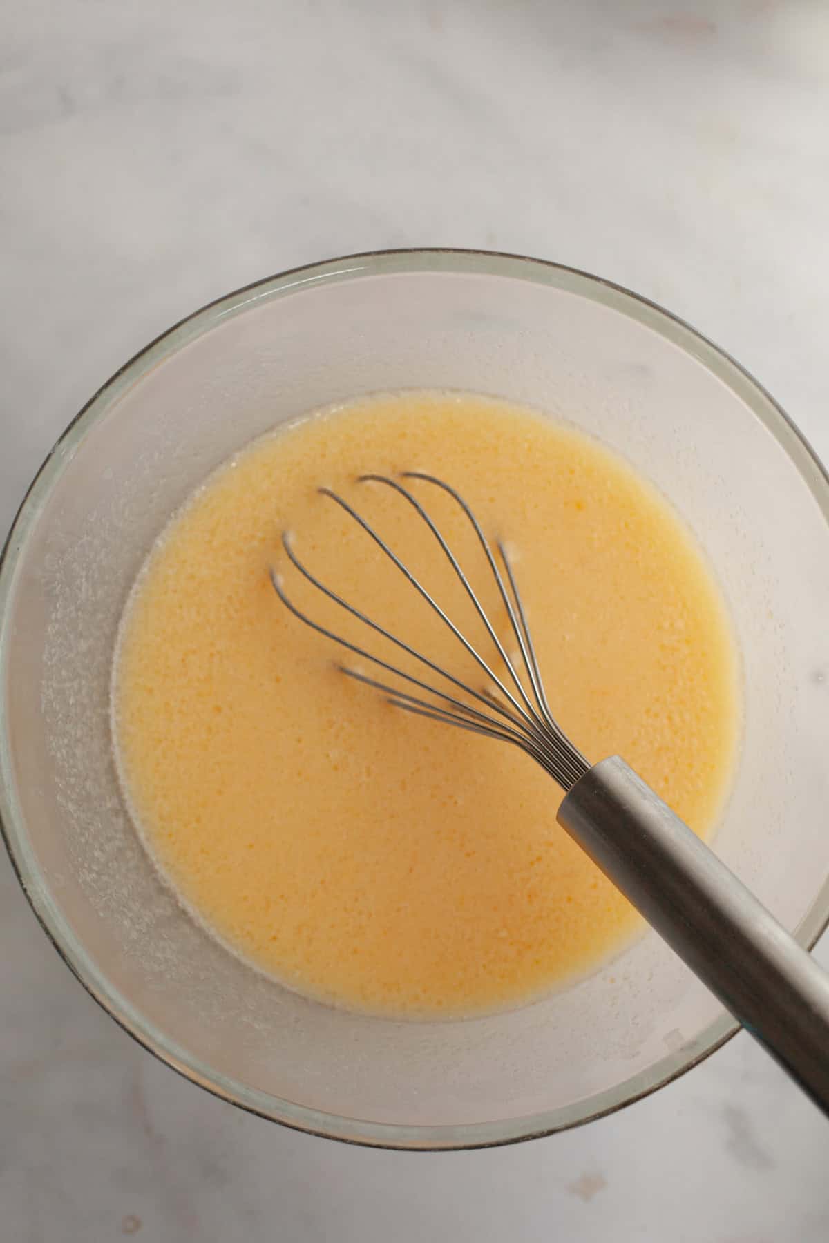 Melted butter, eggs, and sugar in a bowl with a whisk.