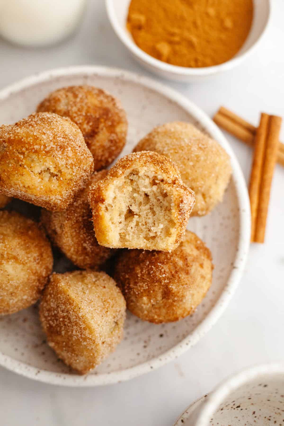 A plate full of cinnamon mini muffins, one has a bite taken out of it.