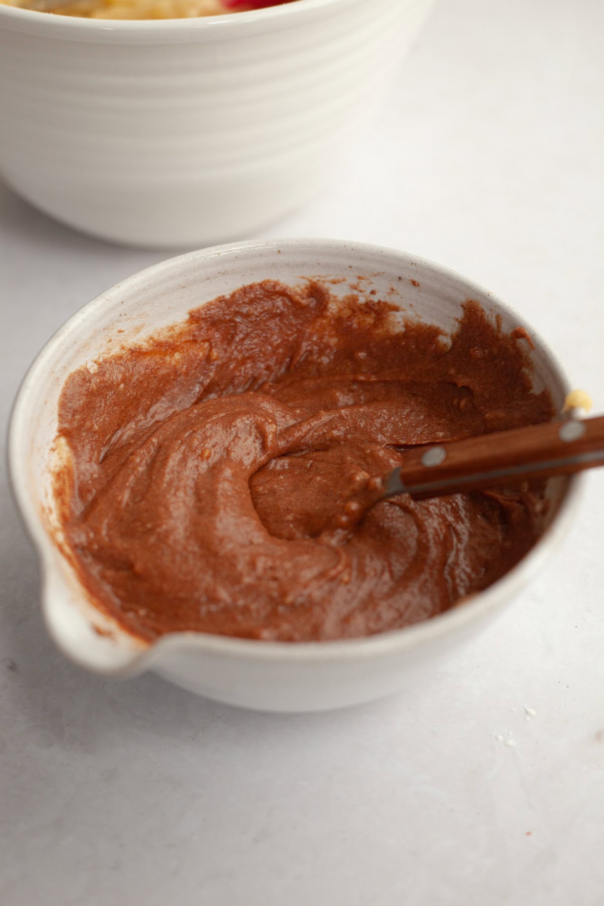 Brown cake batter in a small white bowl with a spoon.