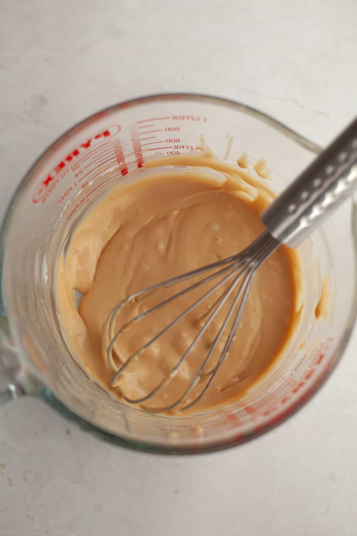 Maple glaze in a glass jug with a whisk.