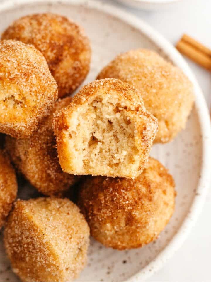 A small plate full of mini cinnamon muffins, one has a bite taken out of it.