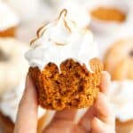 A hand holding a pumpkin cupcake with toasted marshmallow frosting.