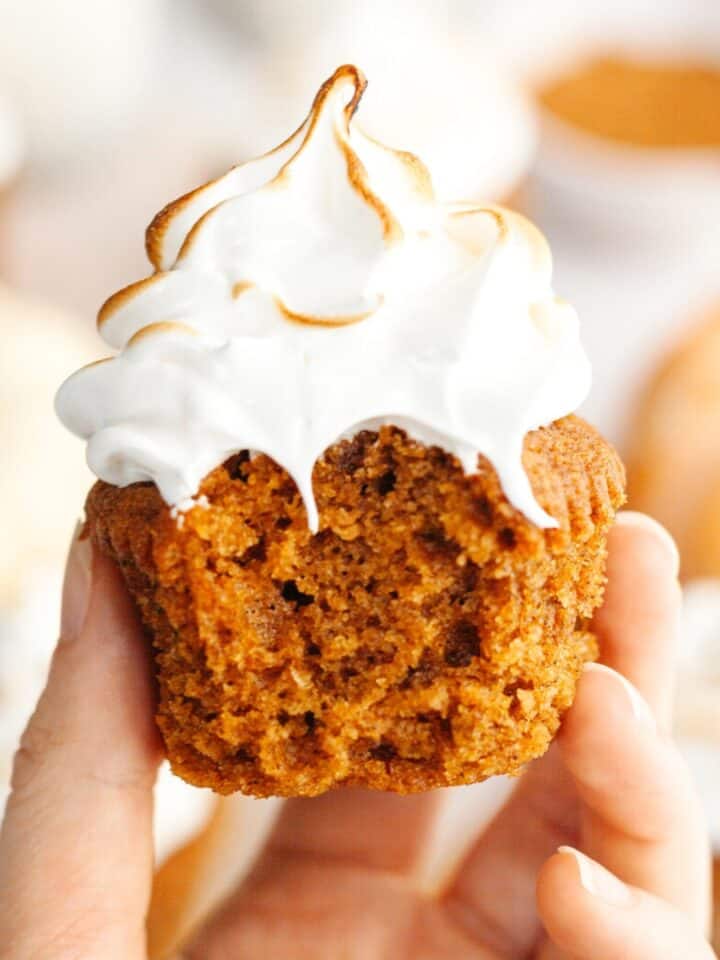 A hand holding a pumpkin cupcake with toasted marshmallow frosting.
