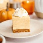 A slice of no bake pumpkin cheesecake on a small plate, topped with whipped cream.