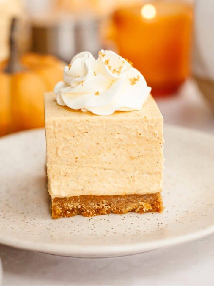 A slice of no bake pumpkin cheesecake on a small plate, topped with whipped cream.