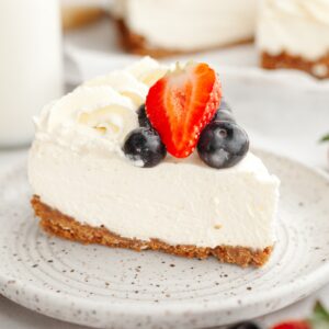 A slice of a no bake vanilla cheesecake topped with fresh blueberries and strawberries on a plate.