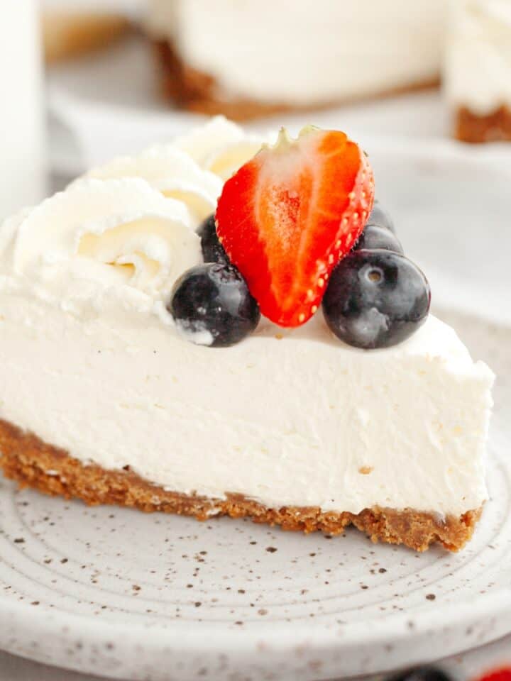 A slice of a no bake vanilla cheesecake topped with fresh blueberries and strawberries on a plate.