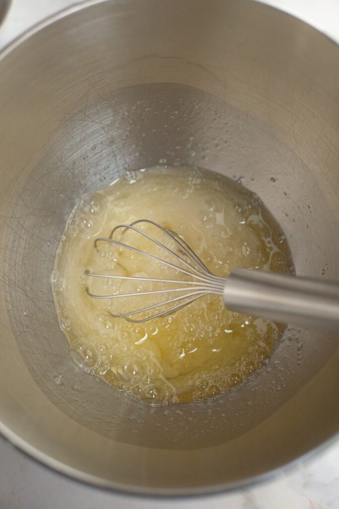 A metal bowl with a whisk and egg whites in it.