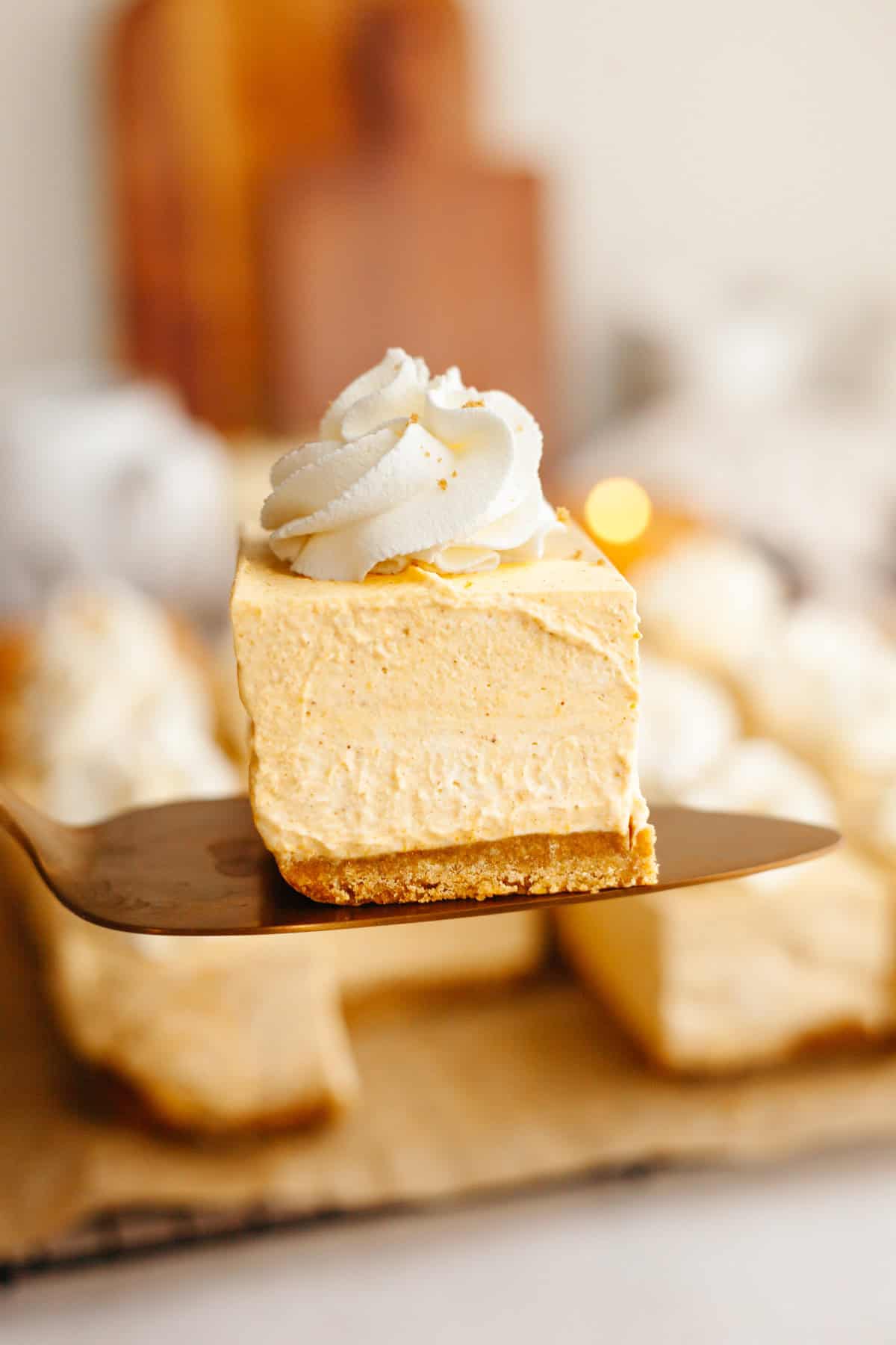 A close up of no bake pumpkin cheesecake bars topped with whipped cream.