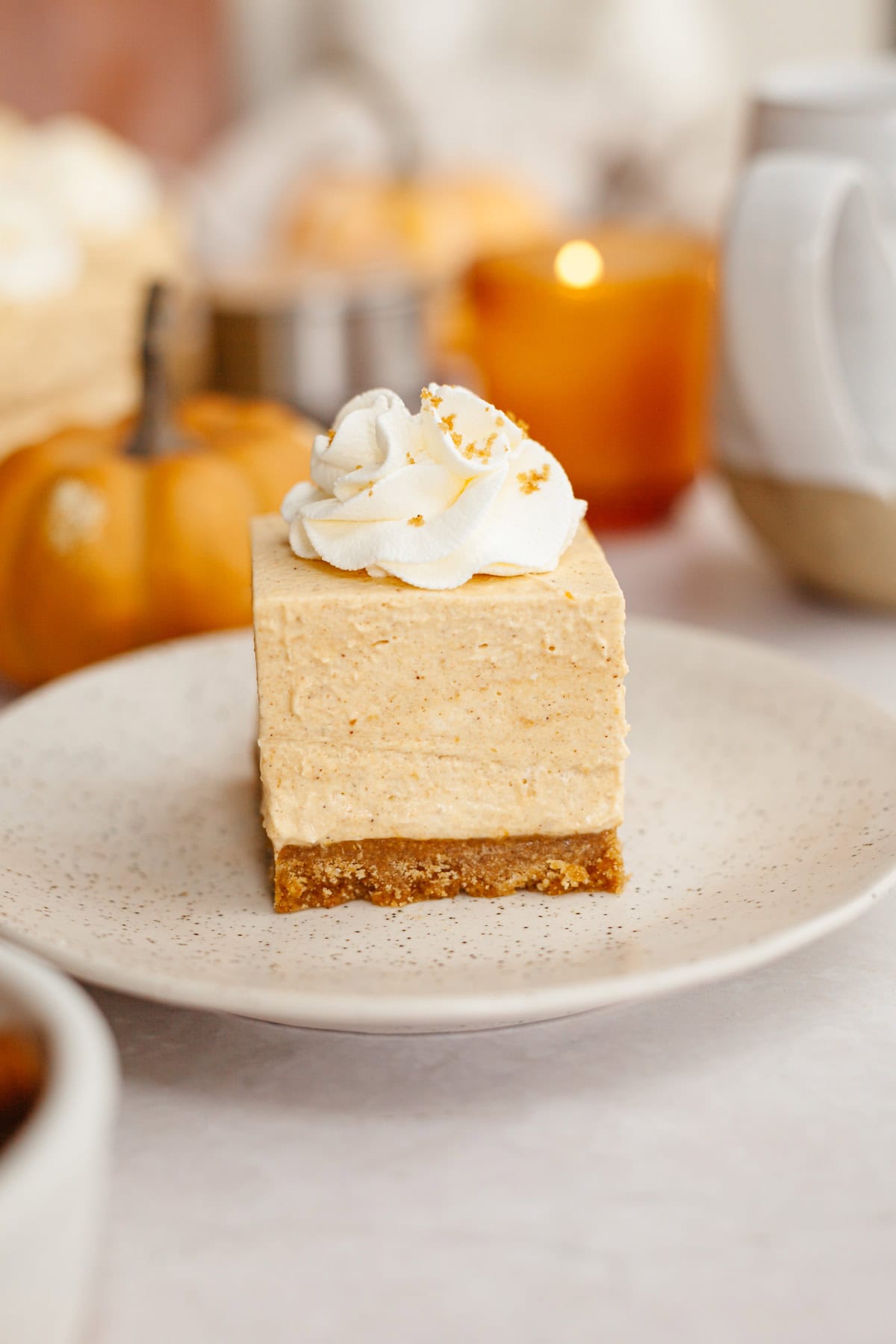 A close up of no bake pumpkin cheesecake bars topped with whipped cream on a small plate.