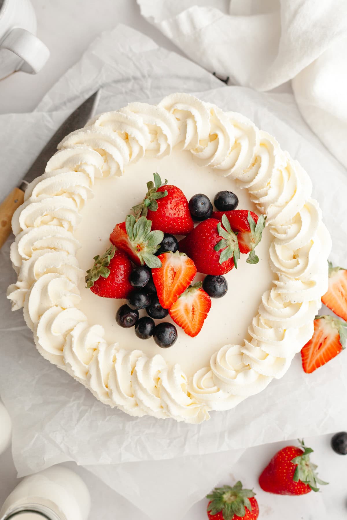 An overhead shot of a vanilla cheesecake piped with whipped cream and decorated with fresh berries.