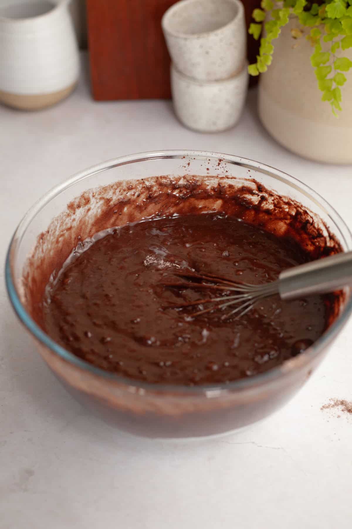 Chocolate cake batter in a glass bowl with a whisk.