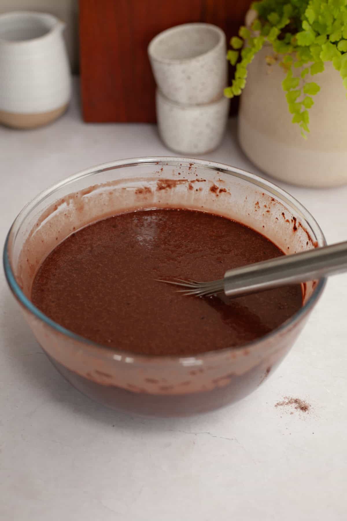 Chocolate cake batter in a glass bowl with a whisk.