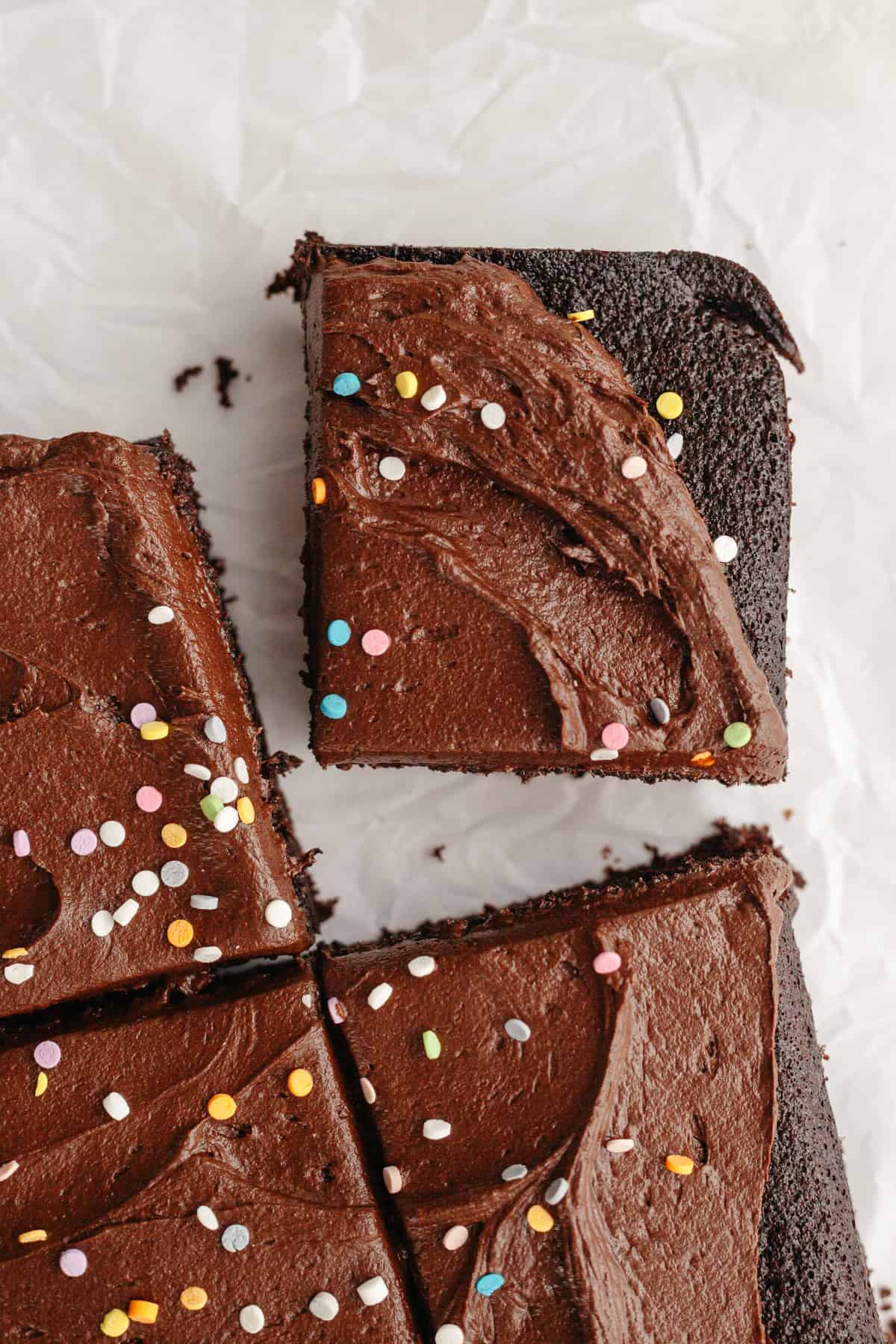 Slices of chocolate sheet cake with chocolate frosting and rainbow sprinkles.