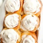 A close up of six cinnamon rolls covered with cream cheese icing.