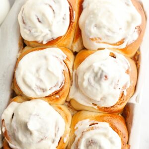 A close up of six cinnamon rolls covered with cream cheese icing.