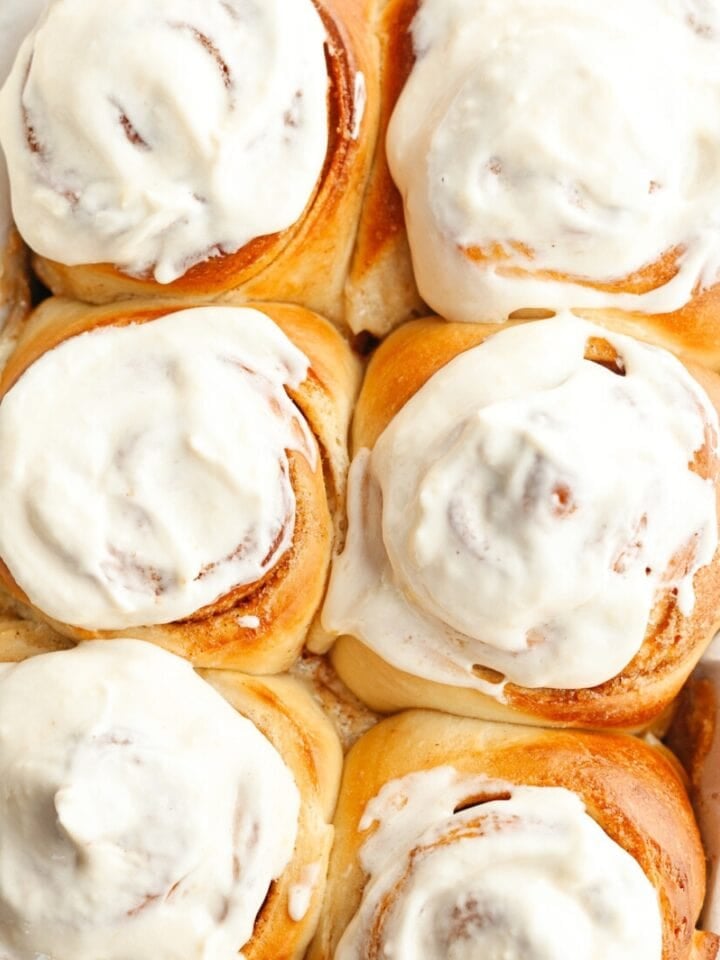 A close up of six cinnamon rolls covered with cream cheese icing.
