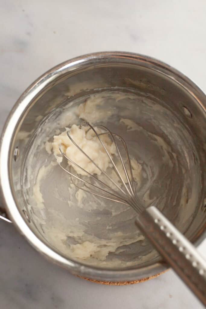 A small silver saucepan with a whisk and tangzhong batter in it.