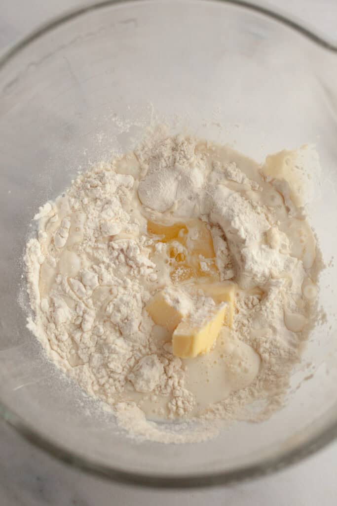 A glass bowl with flour, butter, milk, and yeast.