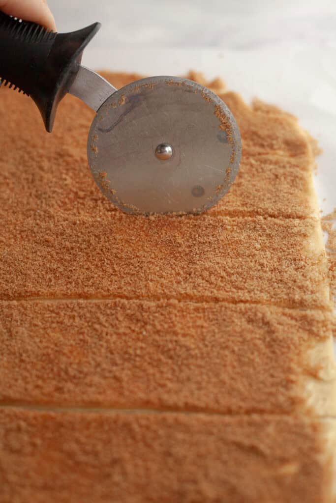 A pizza cutter slicing cinnamon roll dough into strips.