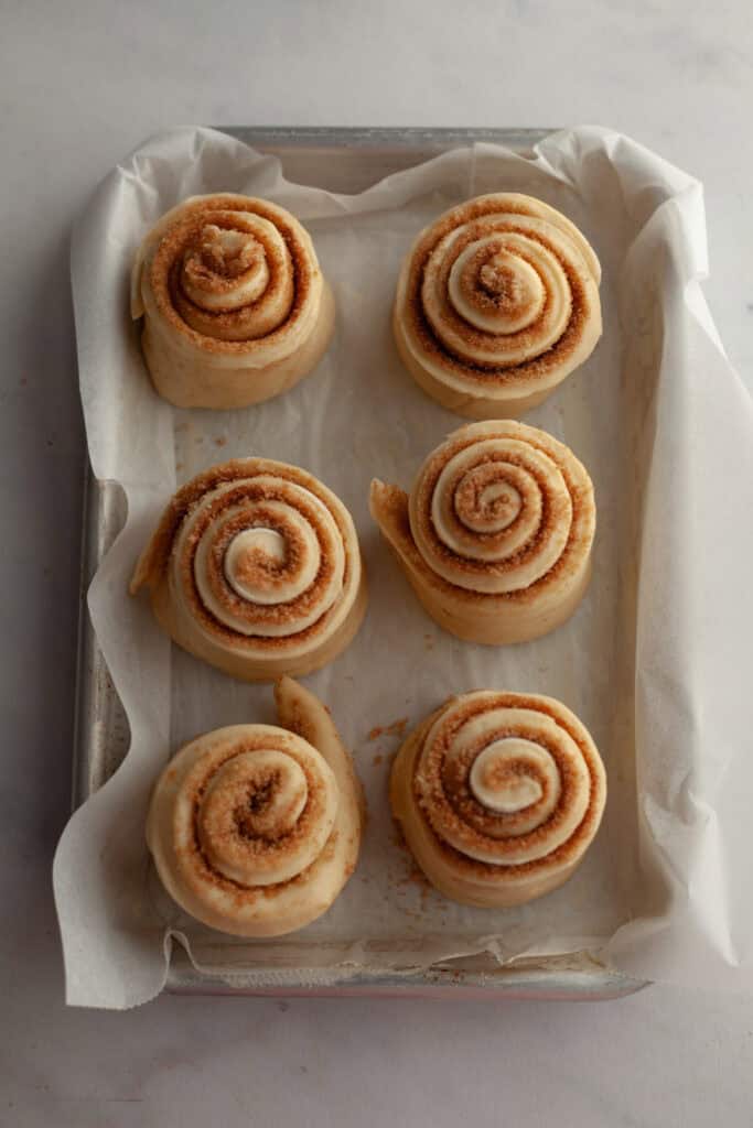 Six cinnamon buns unbaked on a lined sheet pan.