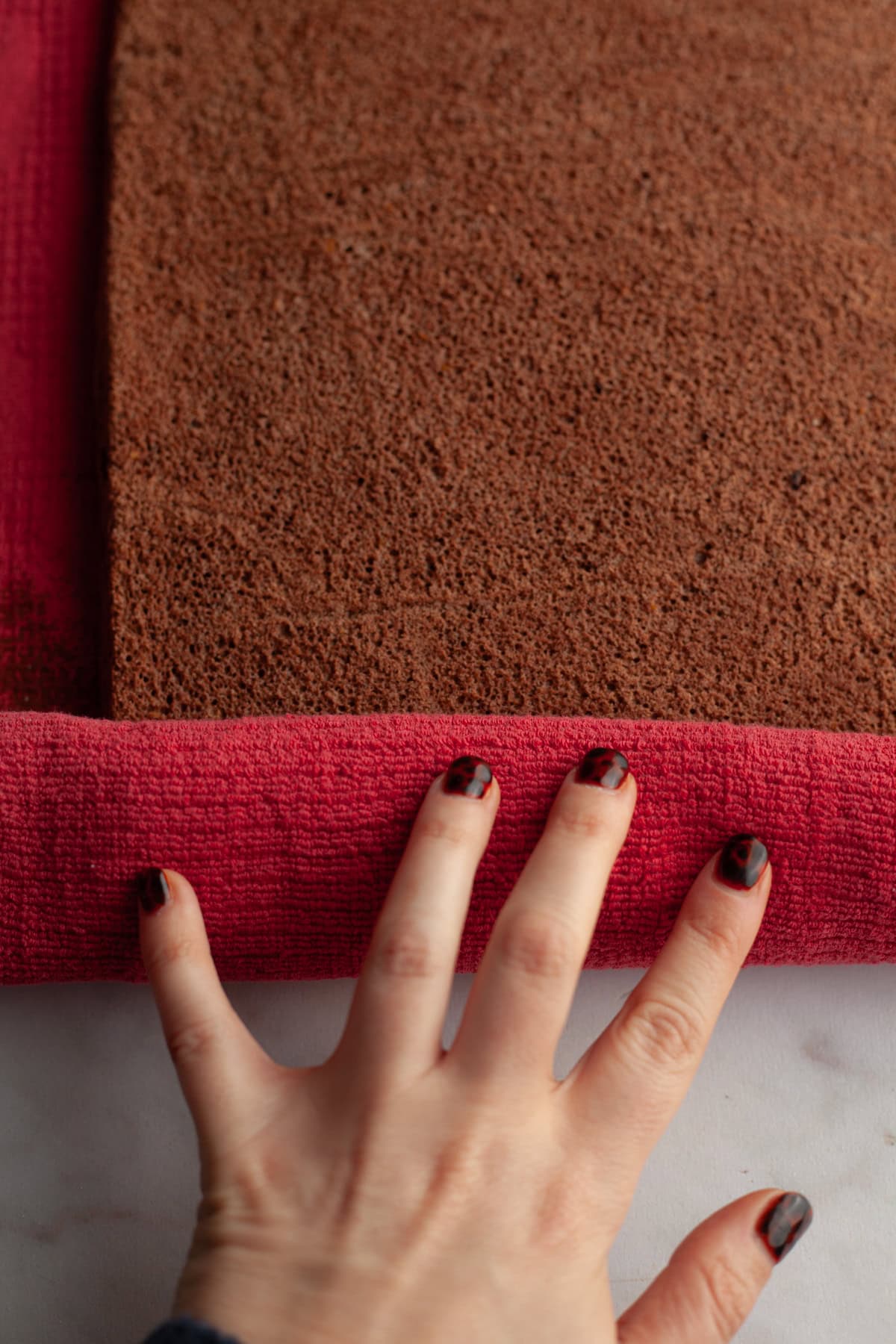 Rolling up a chocolate cake in a red kitchen towel.