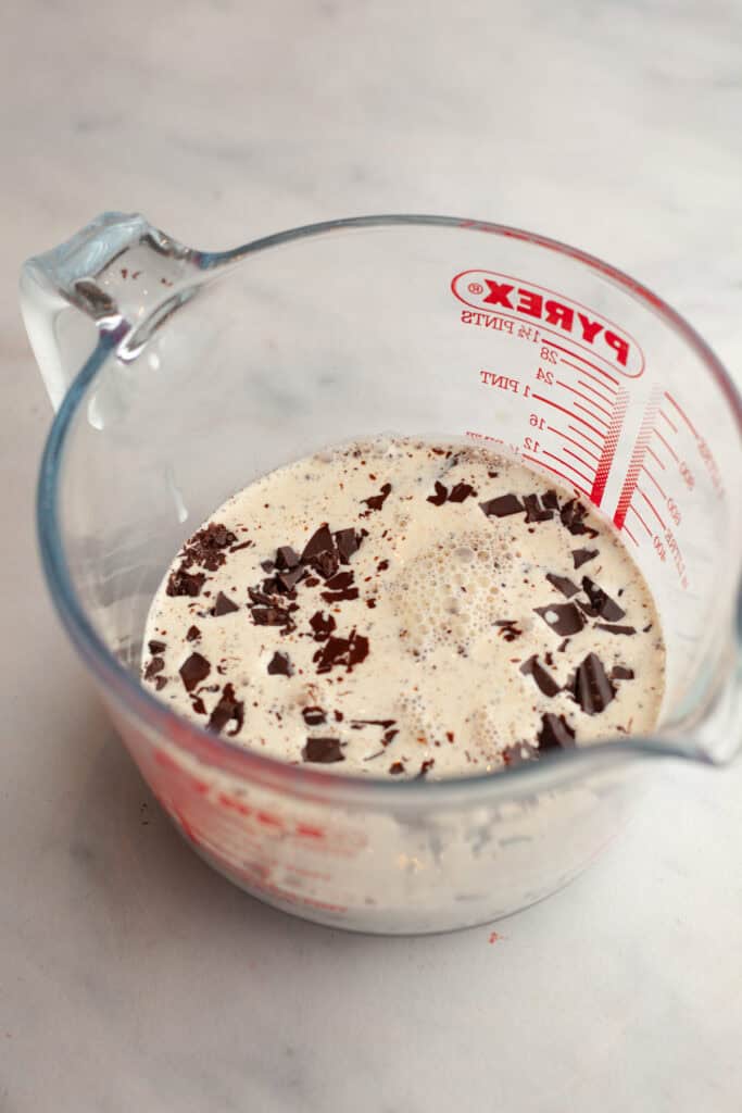 A glass jug with chopped chocolate and cream in it.