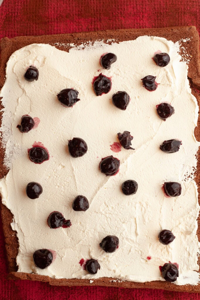 A rectangular chocolate cake, covered in whipped cream and cherries.