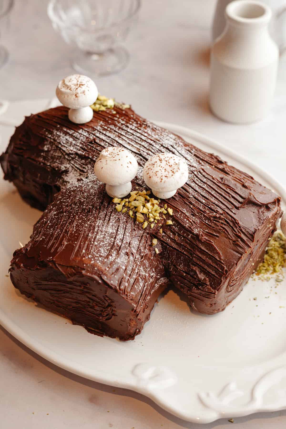 A black forest bûche de noël on a white serving platter, covered in chocolate ganache and meringue mushrooms.