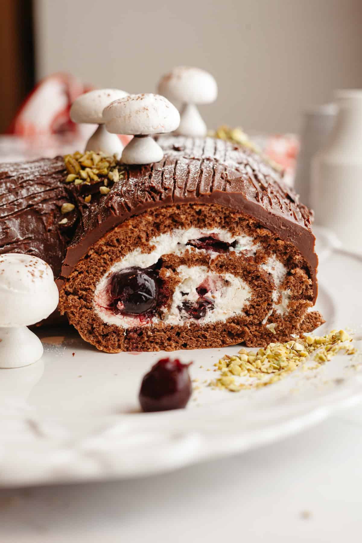 A close up of a sliced black forest yule log with meringue mushrooms on a white plate.