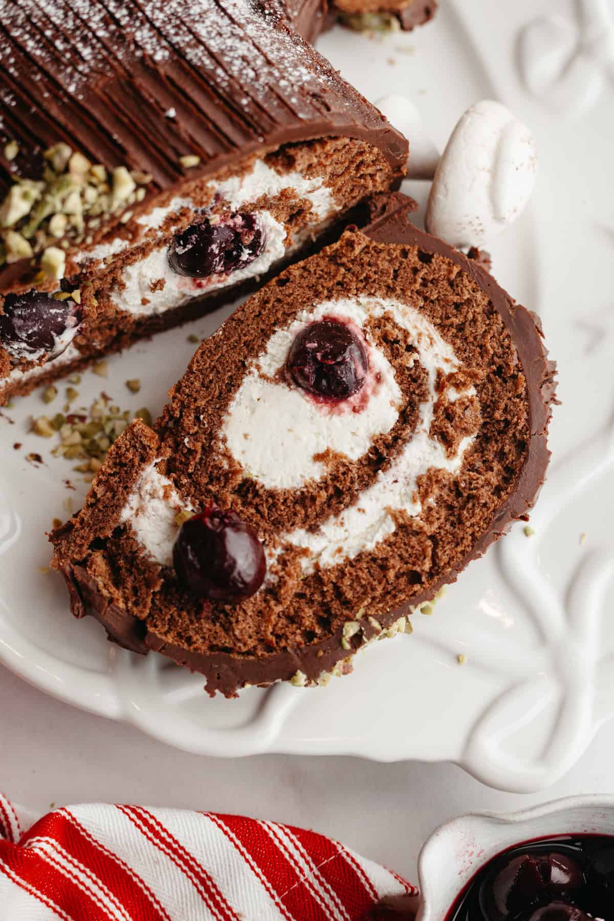 A close up of a slice of black forest yule log on a white serving platter.