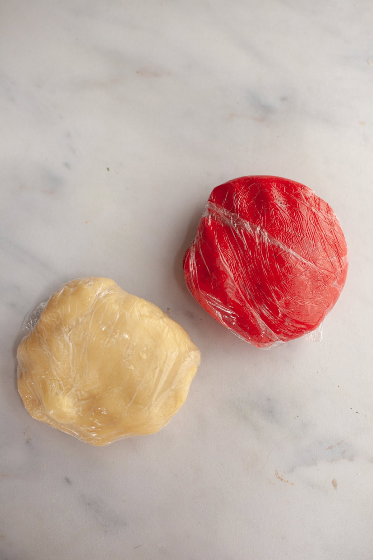 Two discs of shortbread cookie dough wrapped in plastic wrap, one is red and one is beige.