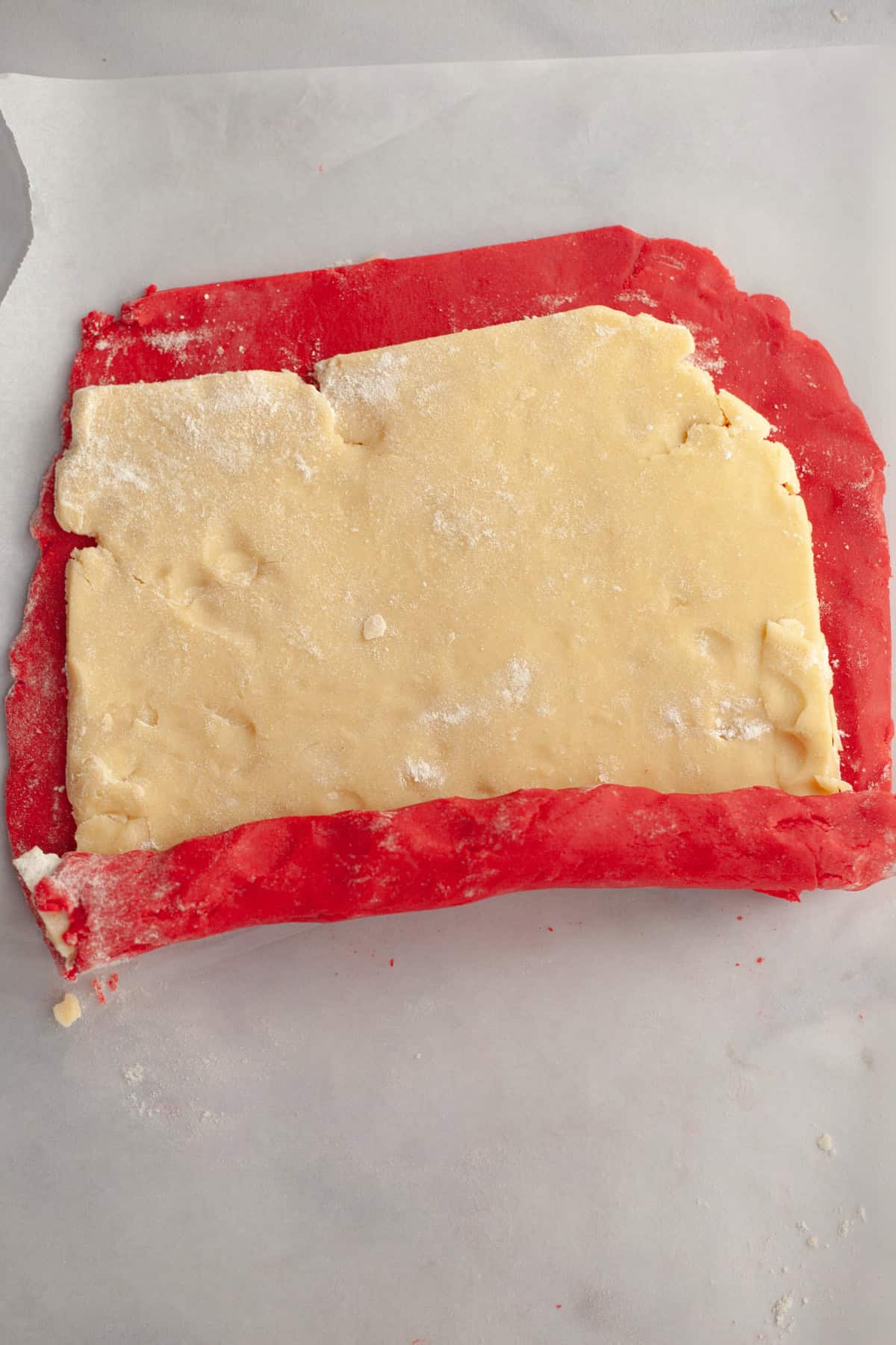 Two pieces of shortbread cookie dough on top of each other, being rolled. One is red and one is beige.